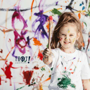 Creative Marketer | A Kid Smiling While Holding A Paint Brush With Paint All Over the Wall And Her Body